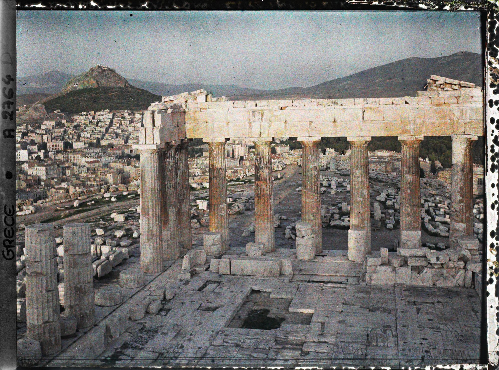 Image représentant Sur l'Acropole, le Parthénon. Vestiges de la colonnade extérieure côté est et derrière eux façade est de l'Acropole, la ville à ses pieds et le Mont Lycabette (vue plongeante)