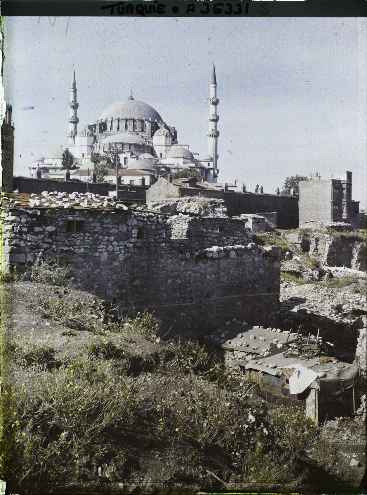 Image représentant La Süleymaniye Camii ("mosquée de Soliman le Magnifique") ; au premier plan des bâtiments couverts d'un toit en toile coincée par des pierres.