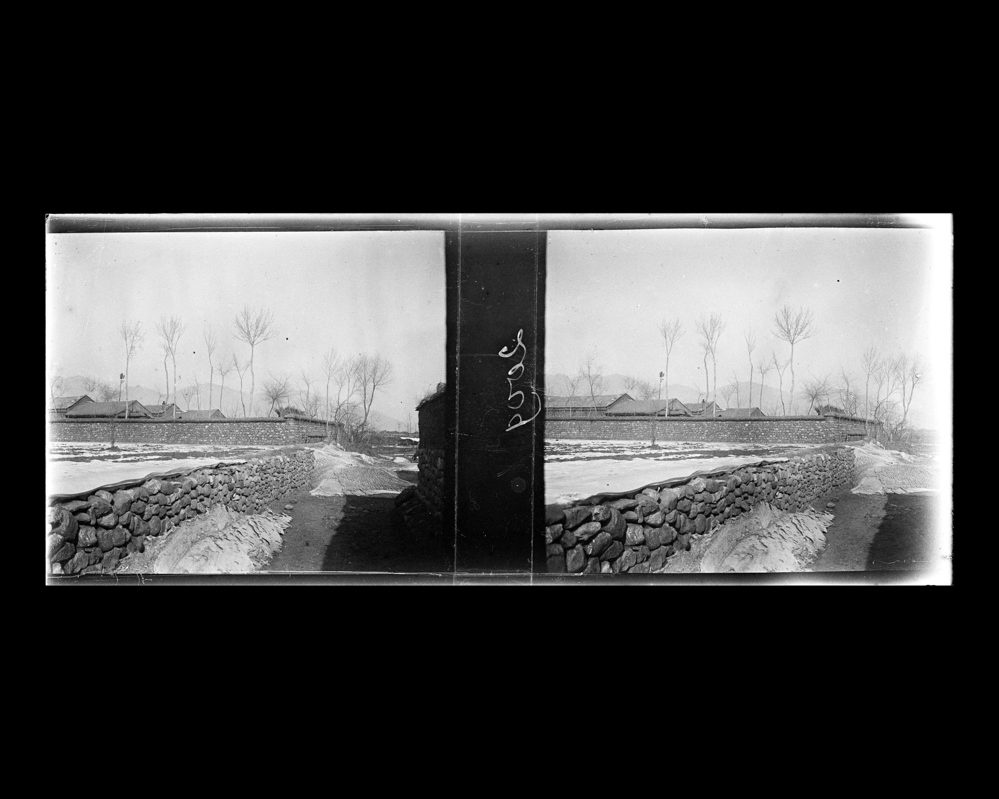 Image représentant Des habitations derrière un mur d'enceinte maçonné peut-être près d'un accès du village