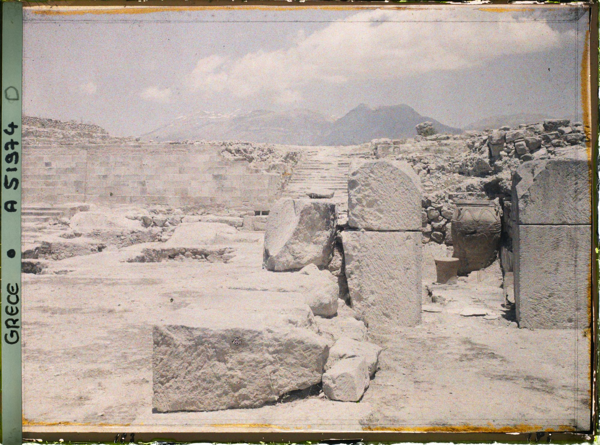 Image représentant Le palais. Dans la cour occidentale, au fond, l'escalier nord. En premier plan, à droite, extrémité des magasins avec un phitos (jarre)