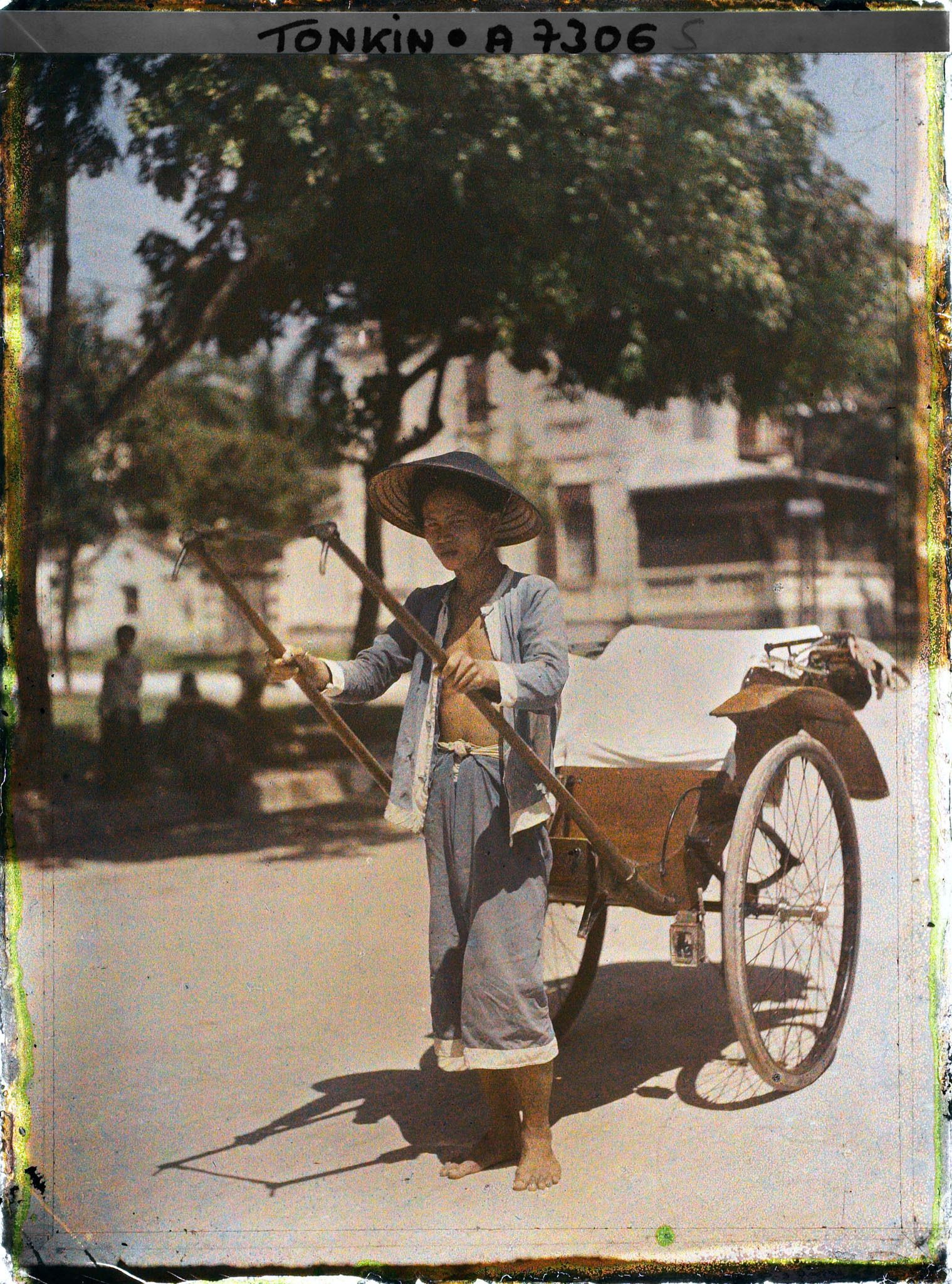Image représentant Un pousse-pousse à roues caoutchoutées et son tireur, vêtu et coiffé de bleu