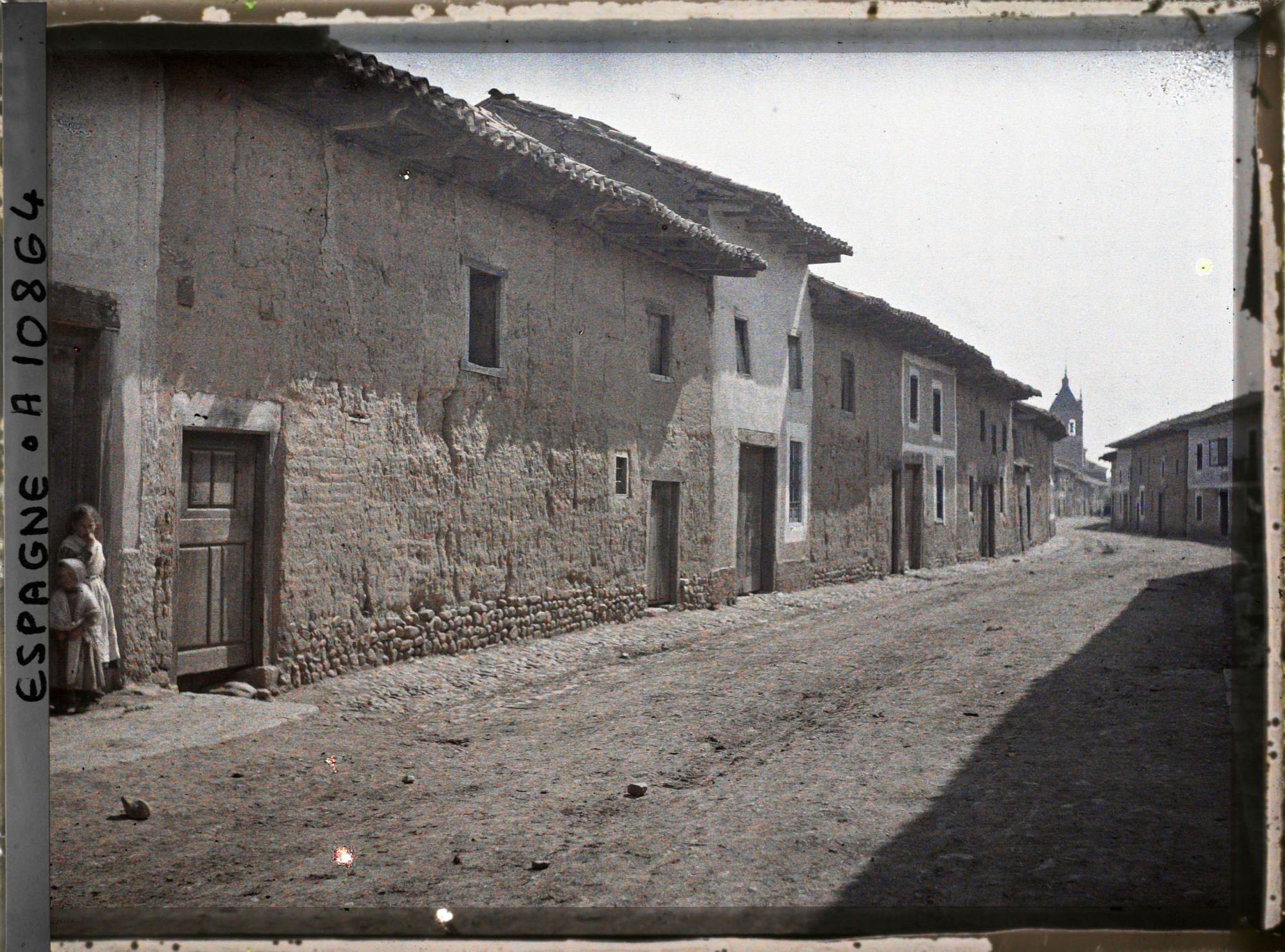 Image représentant Espagne, d'Astorga à Léon, Hospital de Orbigo, la rue et les maisons en terre Crue avec l'Eglise au fond