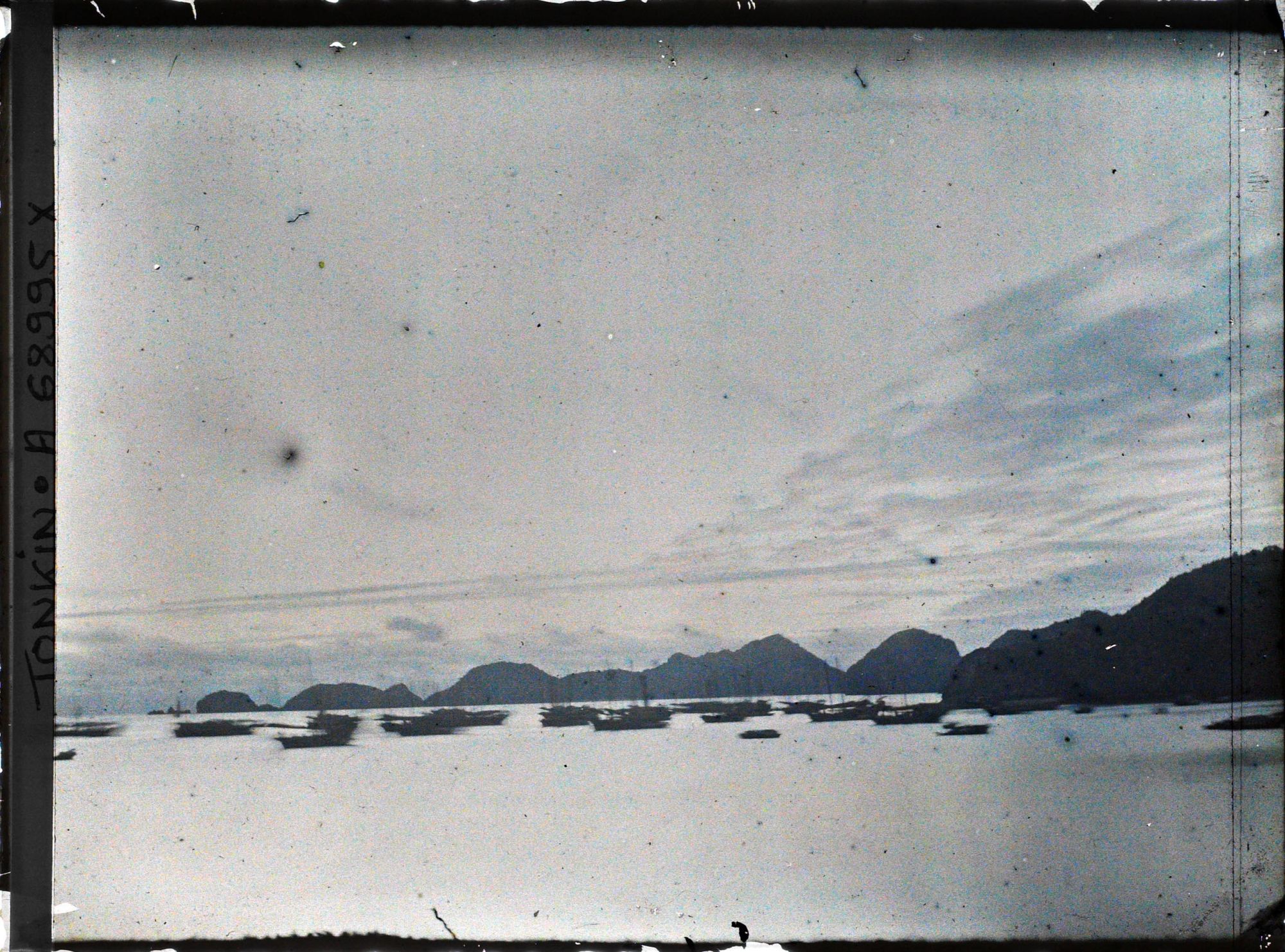 Image représentant Une flottille de sampans et de jonques sur fond de rochers devant l'île Cat-bà, près du poste de douane