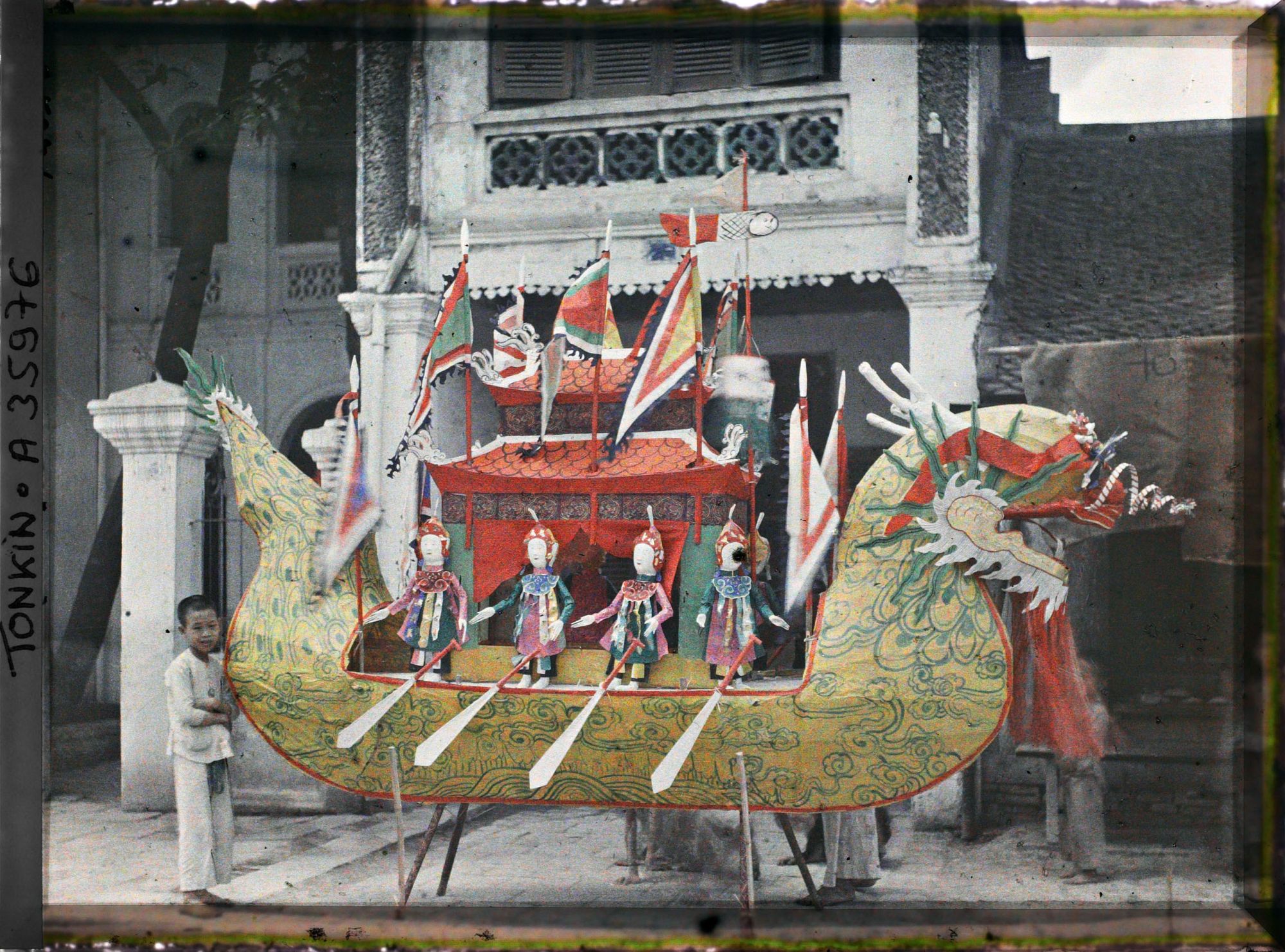 Image représentant Un objet votif en papier, représentant un sampan en forme de dragon, exposé devant un temple (?)