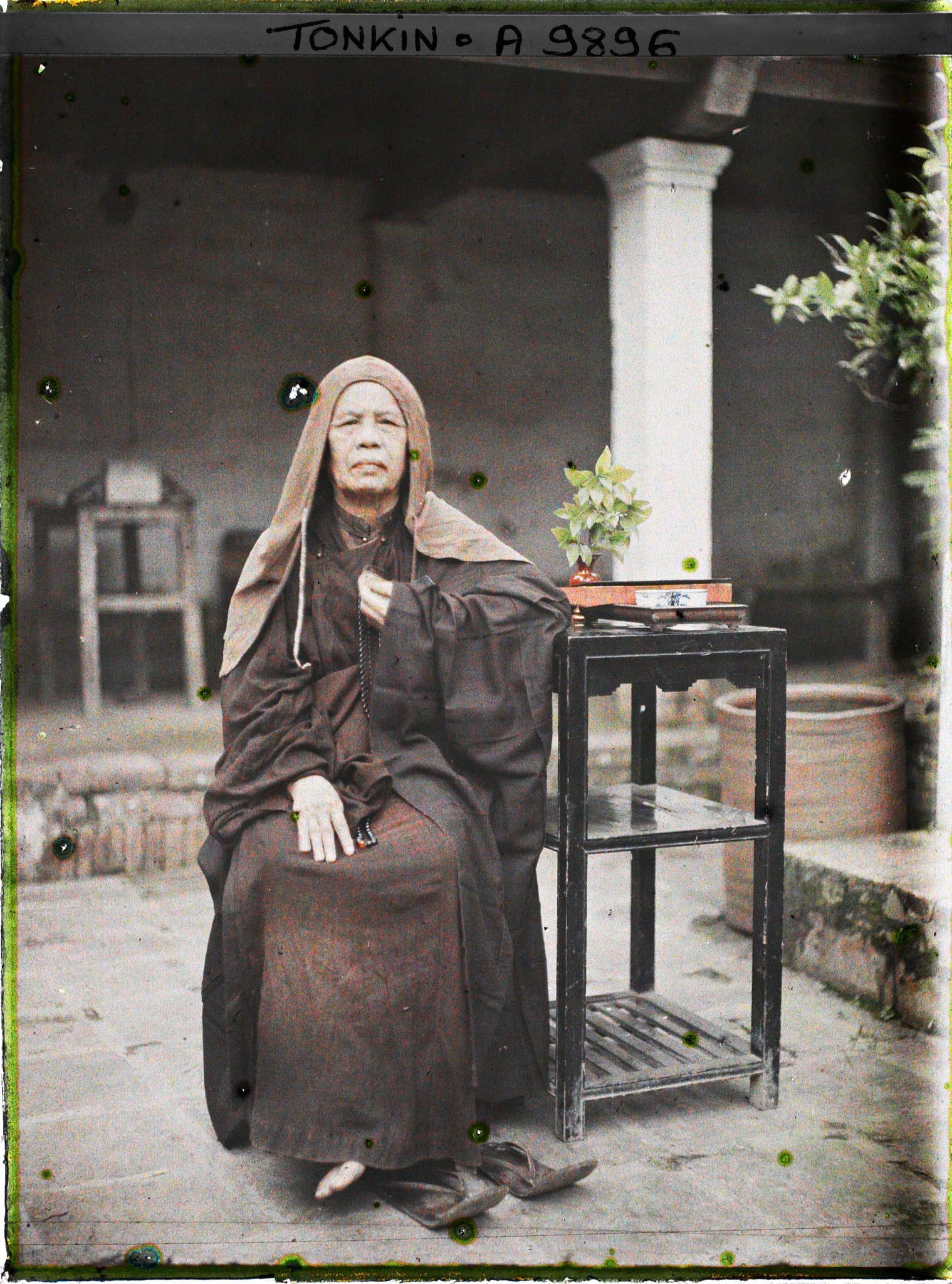 Image représentant Une bonzesse accoudée à une étagère supportant un vase et un service à thé dans la cour intérieure du temple Vien-minh