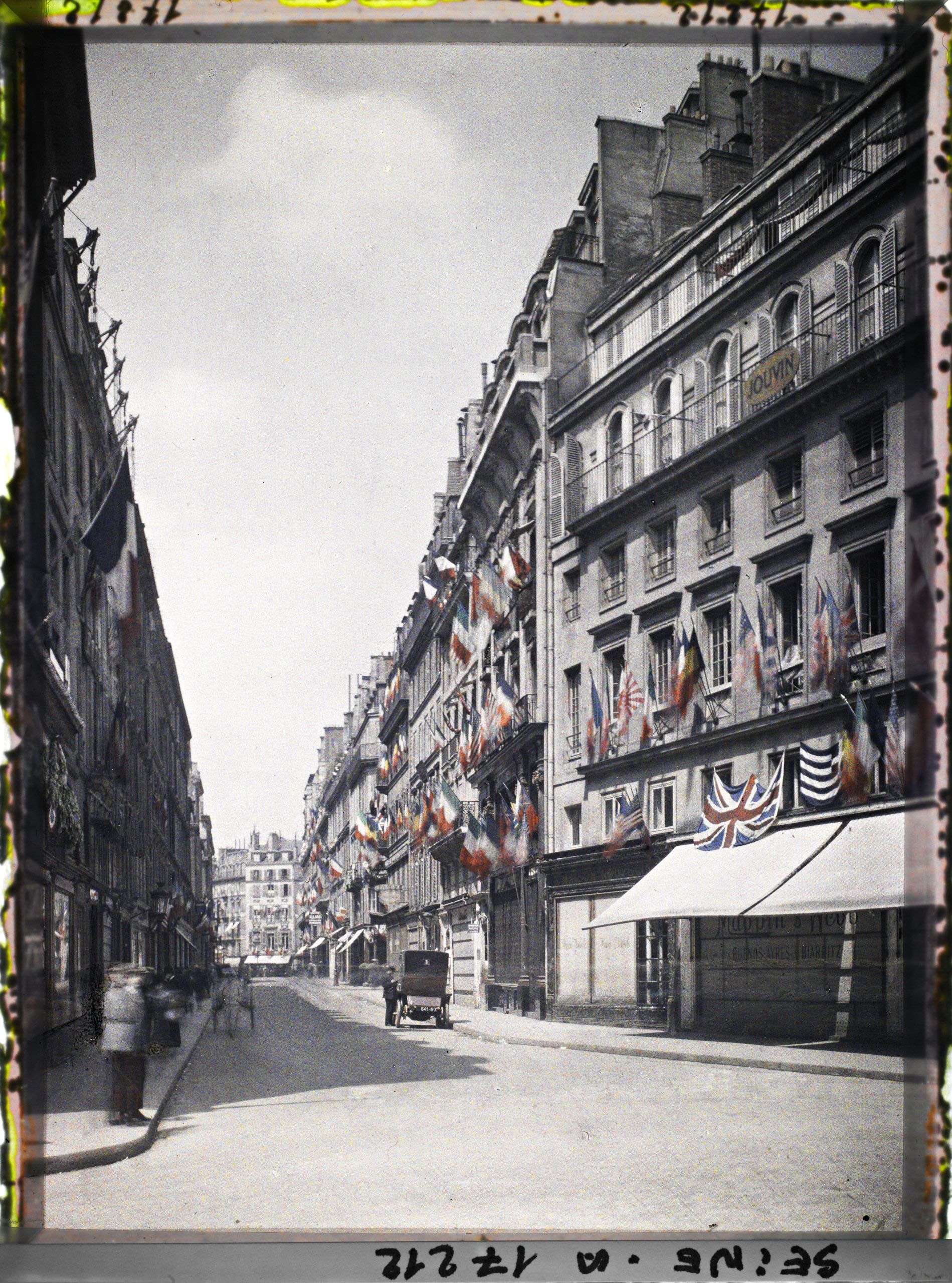 Image représentant La rue des Capucines vue de la rue de la Paix et décorée des drapeaux alliés pour les fêtes de la Victoire des 13 et 14 juillet 1919