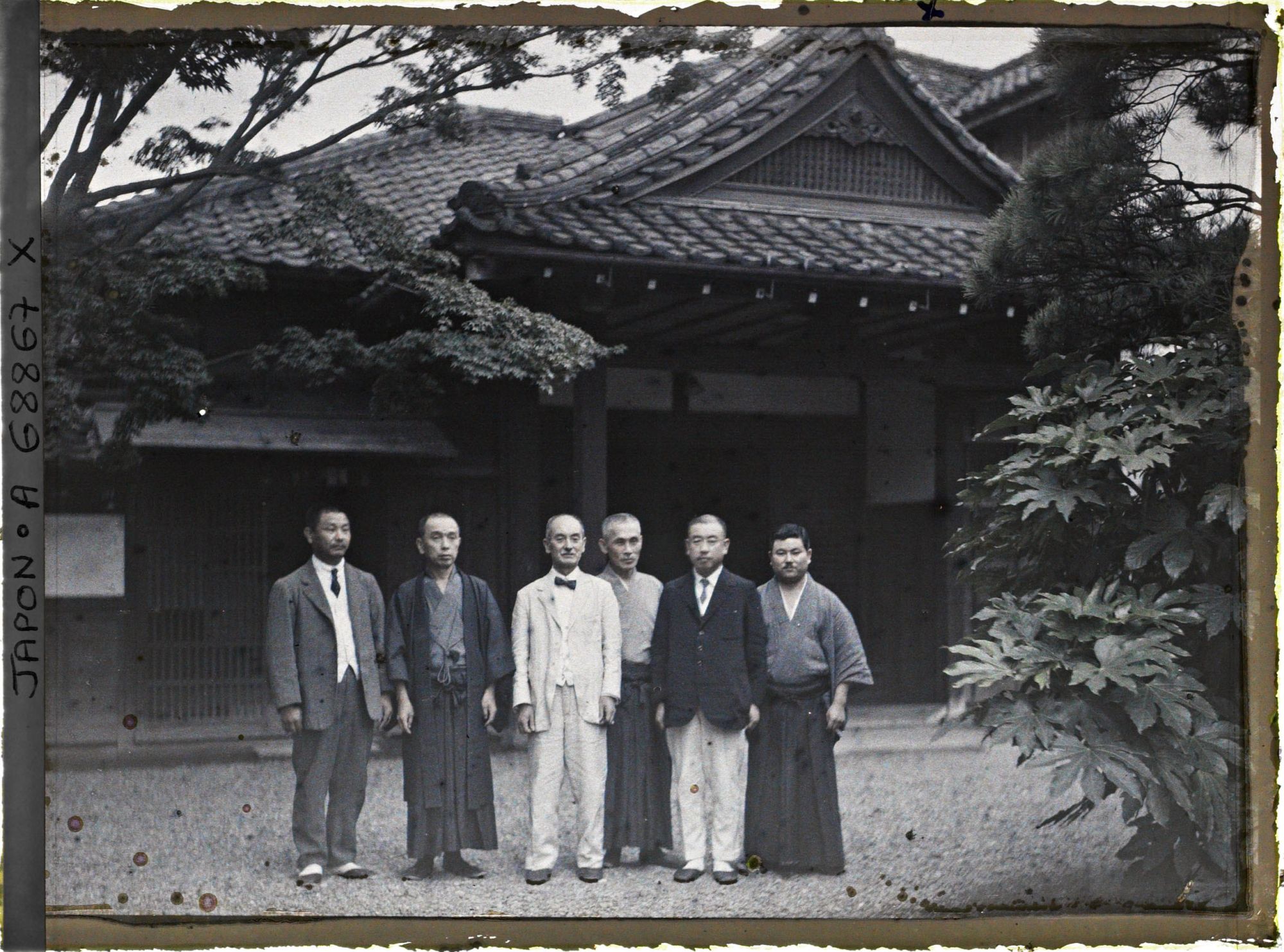 Image représentant Groupe d'hommes, les uns en vêtements traditionnels, les autres habillés à l'occidentale, devant une résidence non identifiée
