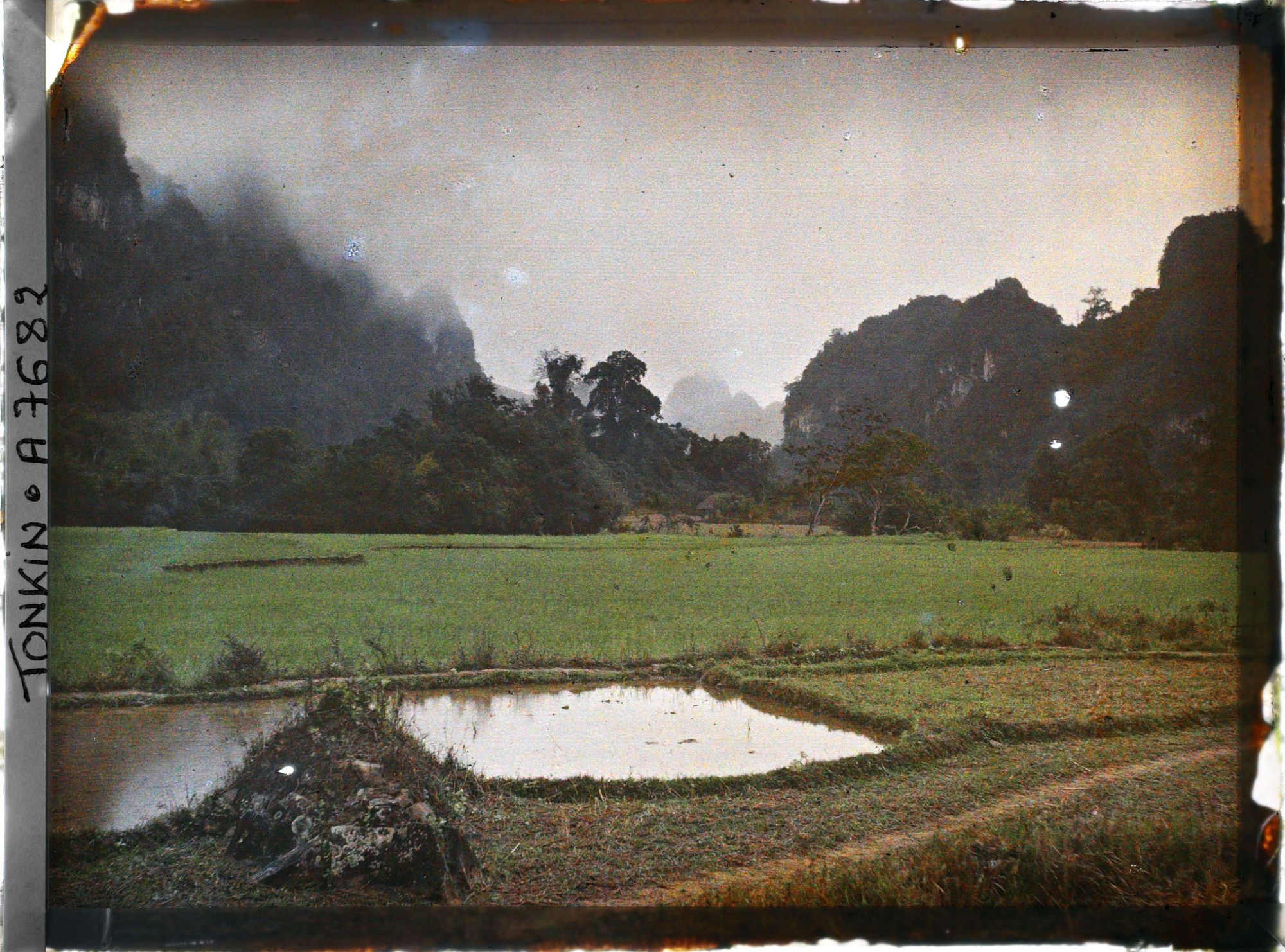 Image représentant Des rizière au pied des rochers, à gauche au premier plan, un tombeau Mnong