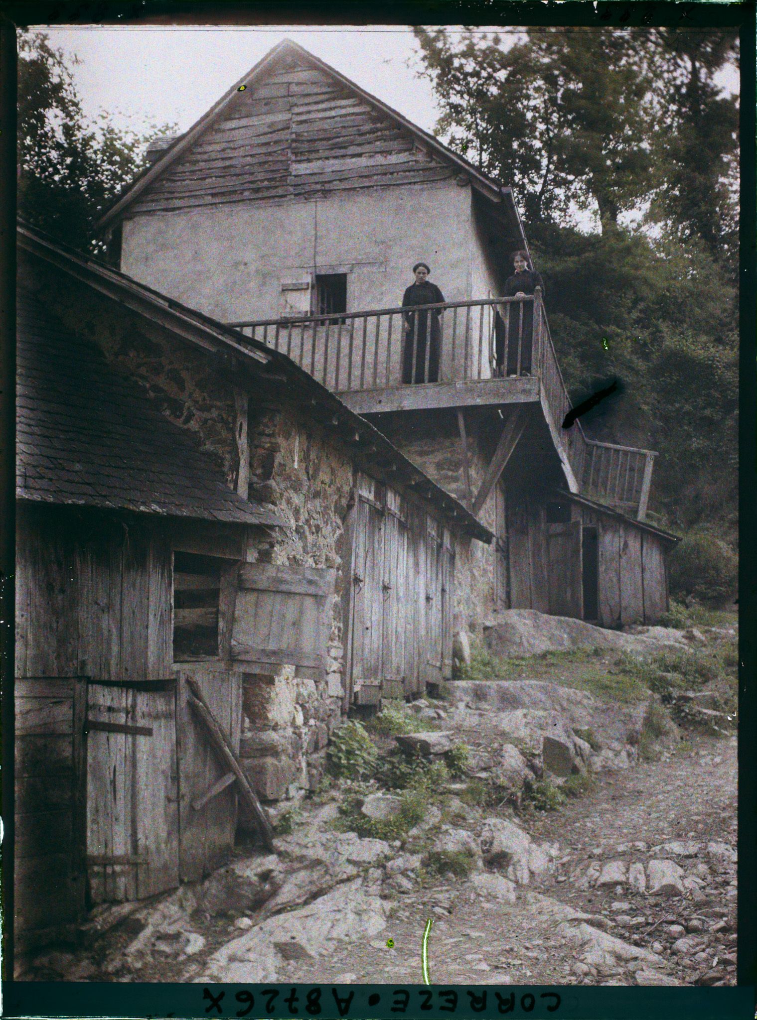 Image représentant Une maison rurale avec loges à cochons au rez de chaussée avec deux femmes au balcon