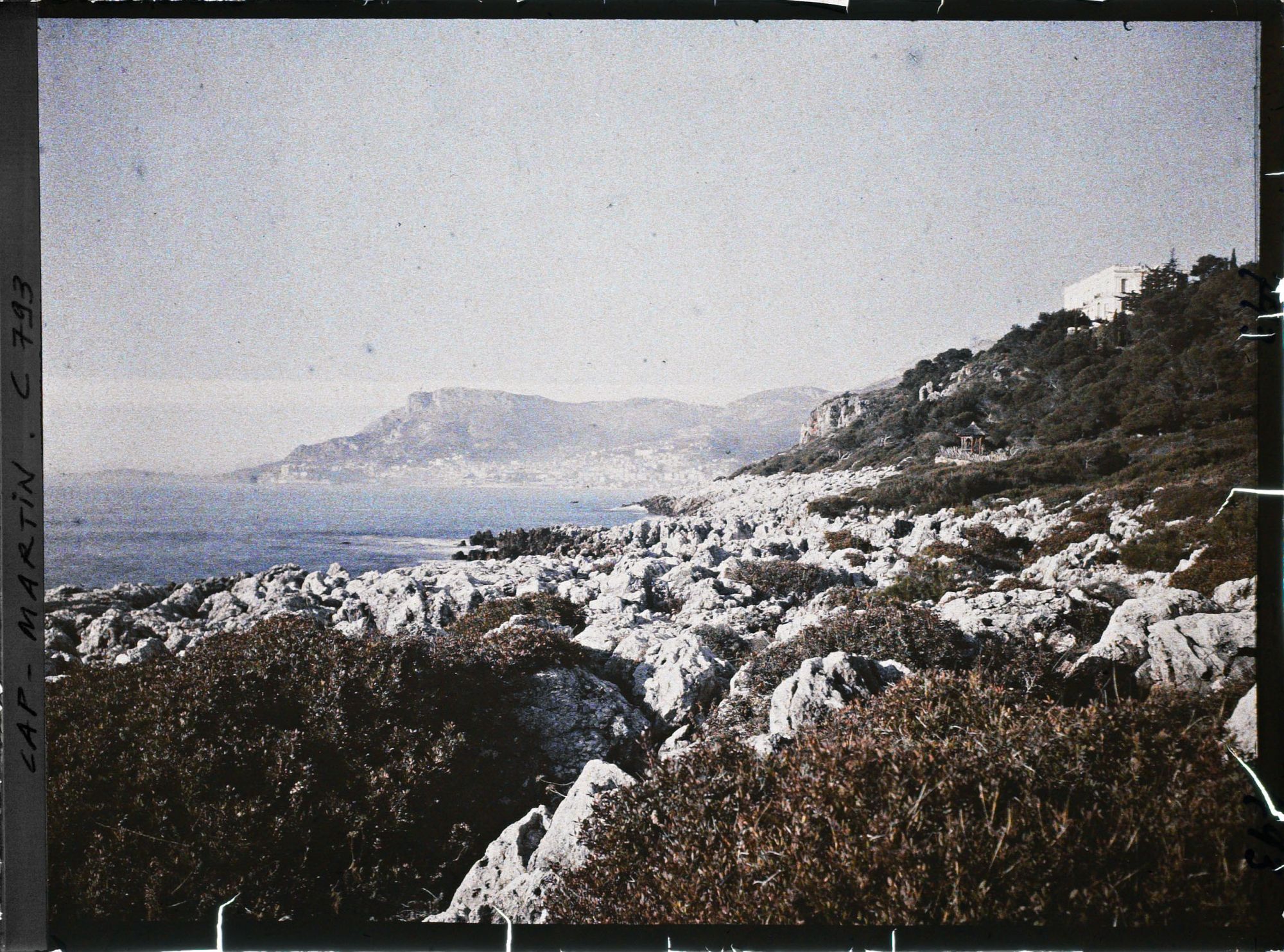 Image représentant La villa Kahn dite villa Zamir, vue depuis le rivage où roches et végétation se mêlent
