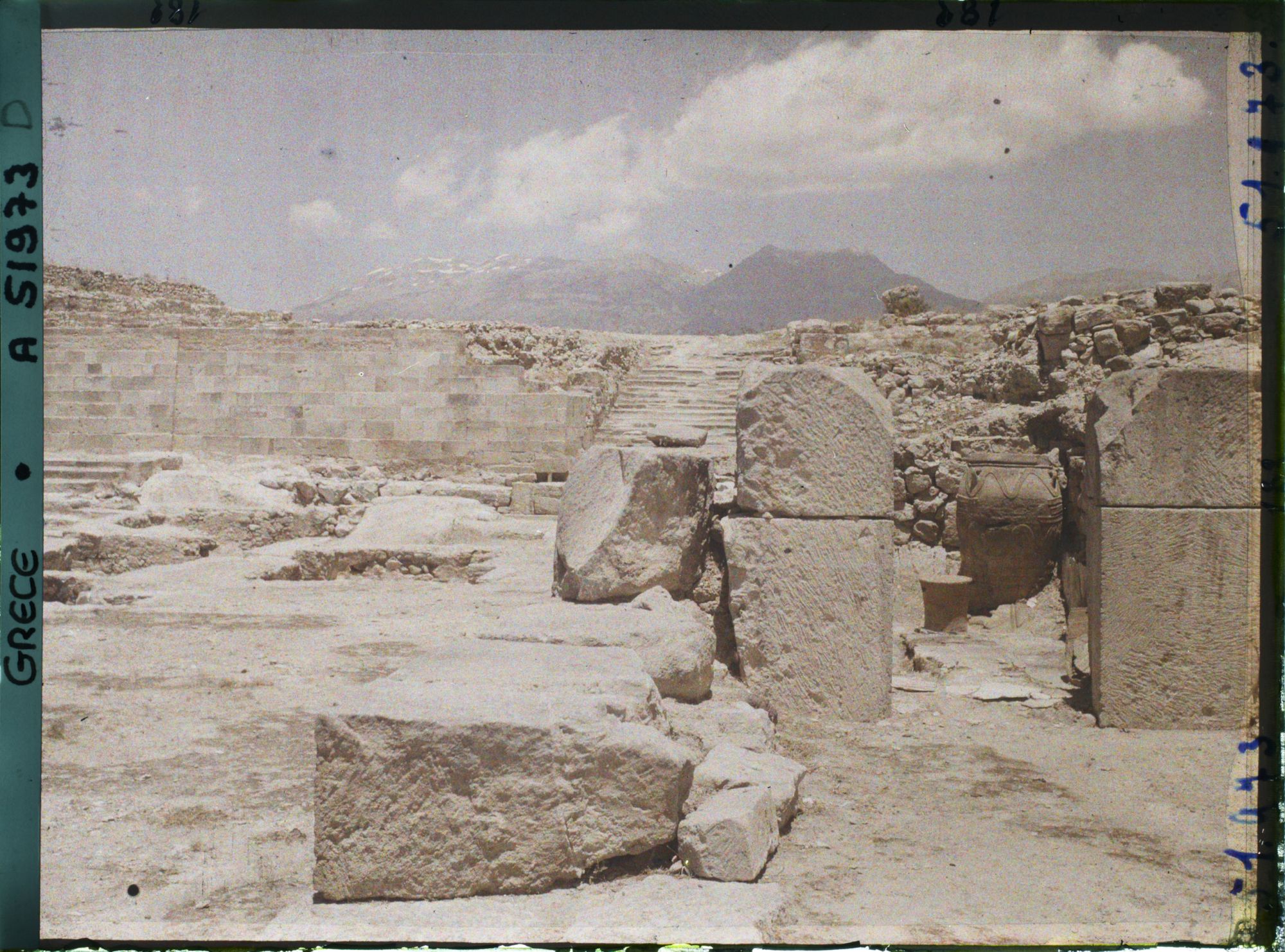 Image représentant Le palais. Dans la cour occidentale, au fond, l'escalier nord. En premier plan, à droite, extrémité des magasins avec un phitos (jarre)