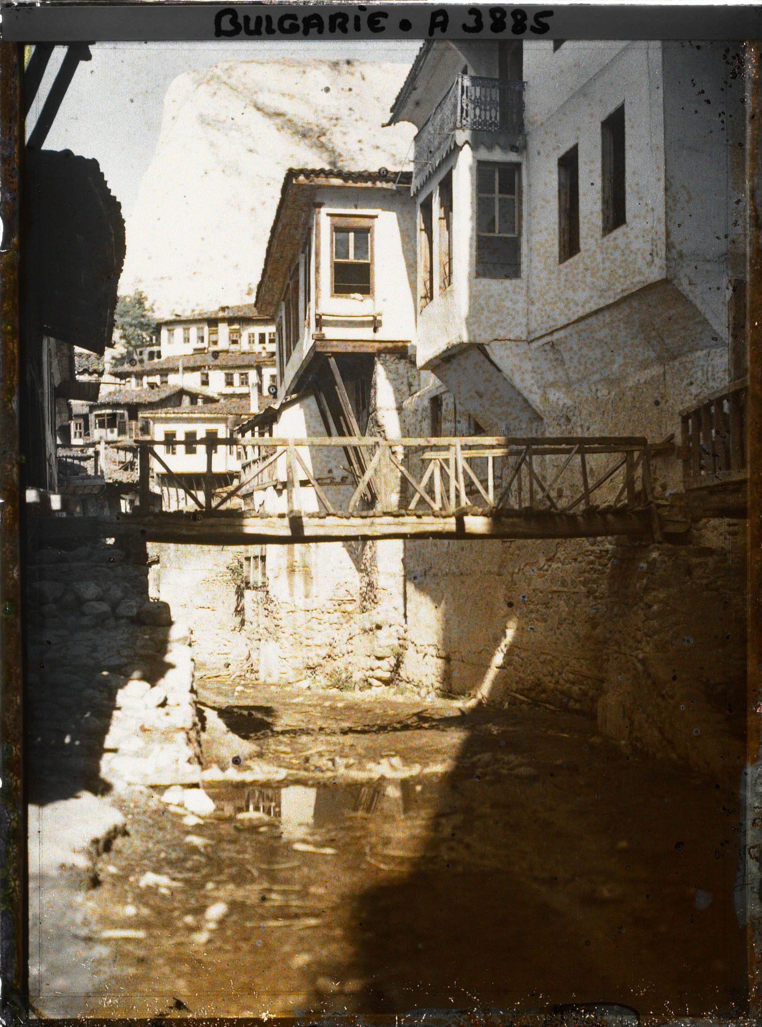 Image représentant Petit pont de bois enjambant une rue de terre battue et bordée de maisons en étages