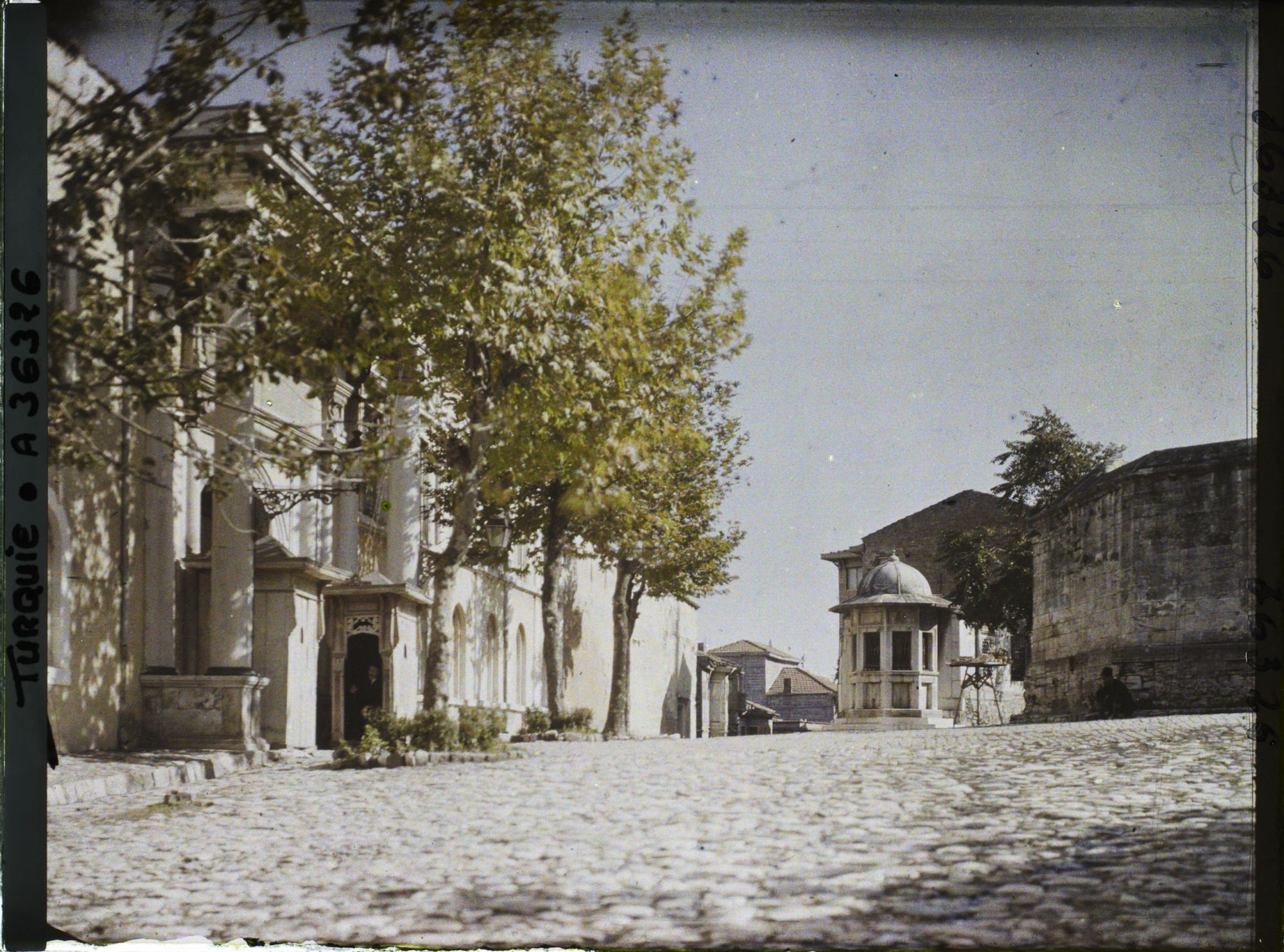 Image représentant Sur une place pavée, à gauche, entrée monumentale d'un palais, encadrée de deux guérites ("Palais du Cheikh-ul-Islam" ou mufti, premier dignitaire de l'église musulmane ottomane)