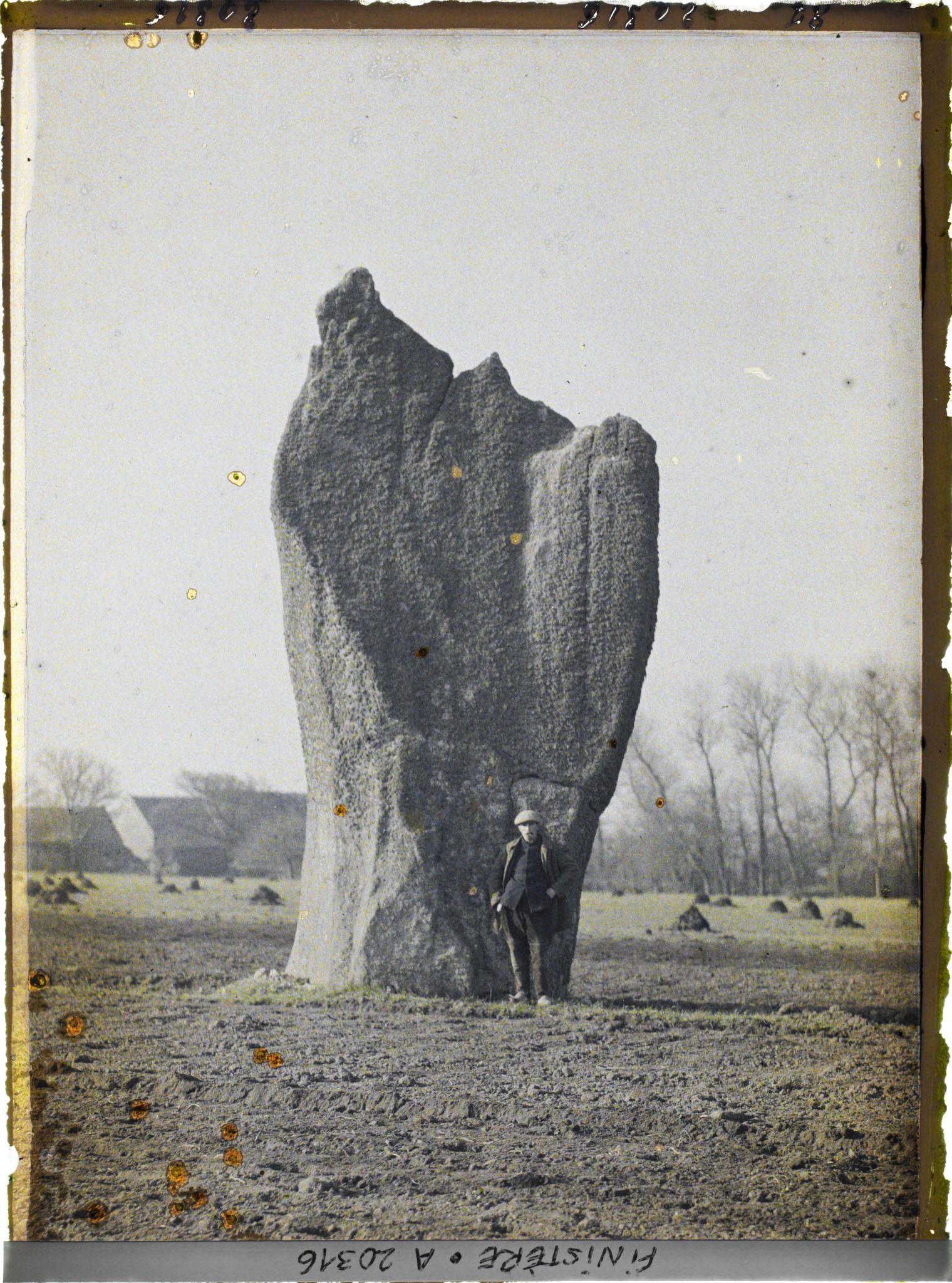 Image représentant Devant l'un des deux menhirs de Kerscaven, dit le menhir de l'Evêque, un homme pose pour indiquer l'echelle du mégalithe