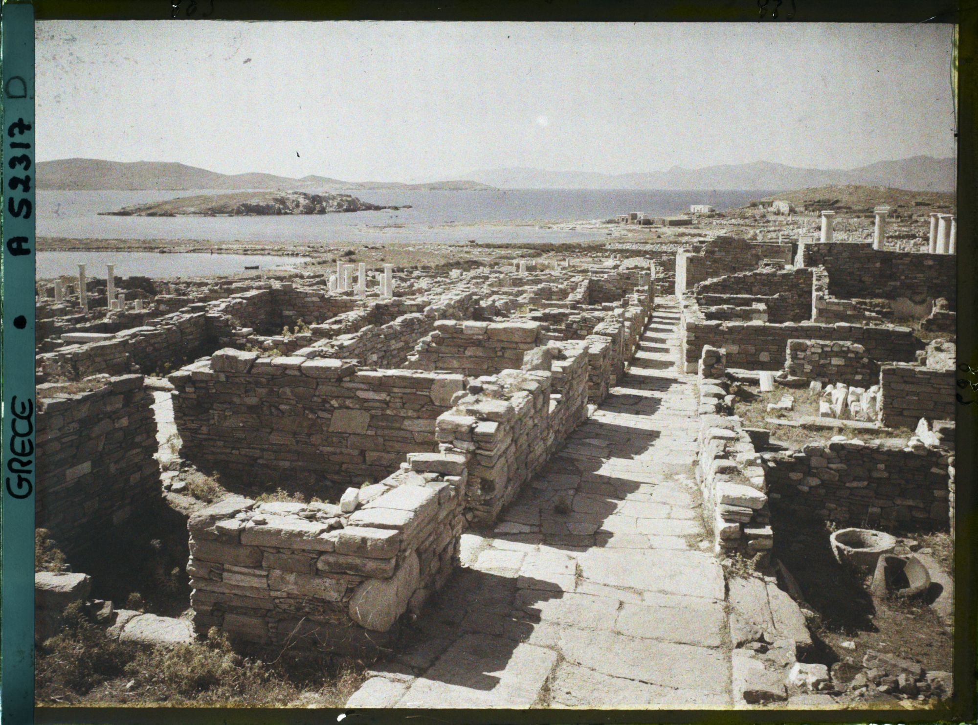 Image représentant La rue du Théâtre, vue vers la ville basse. Au fond, l'ile de Tinos