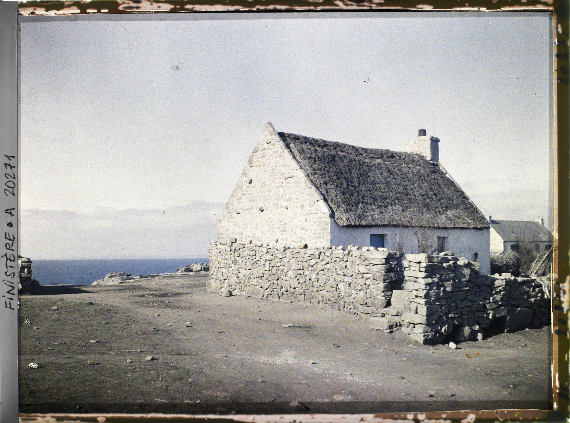 Image représentant Une maison aux murs chaulés et au toit couvert de chaume, entourée d'un muret