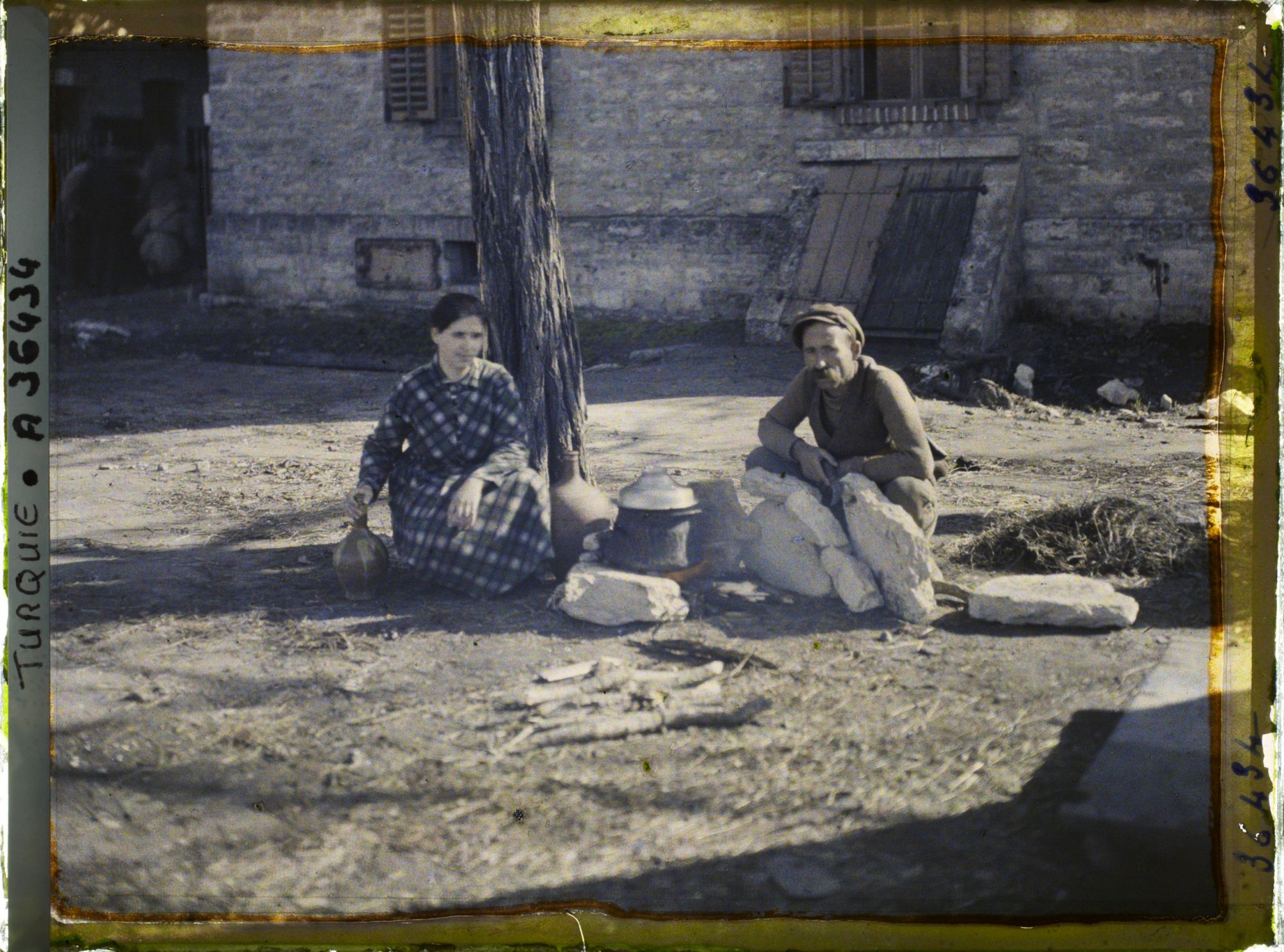 Image représentant Un homme et une jeune femme grecs s'apprêtant à quitter la ville prêt d'un foyer improvisé