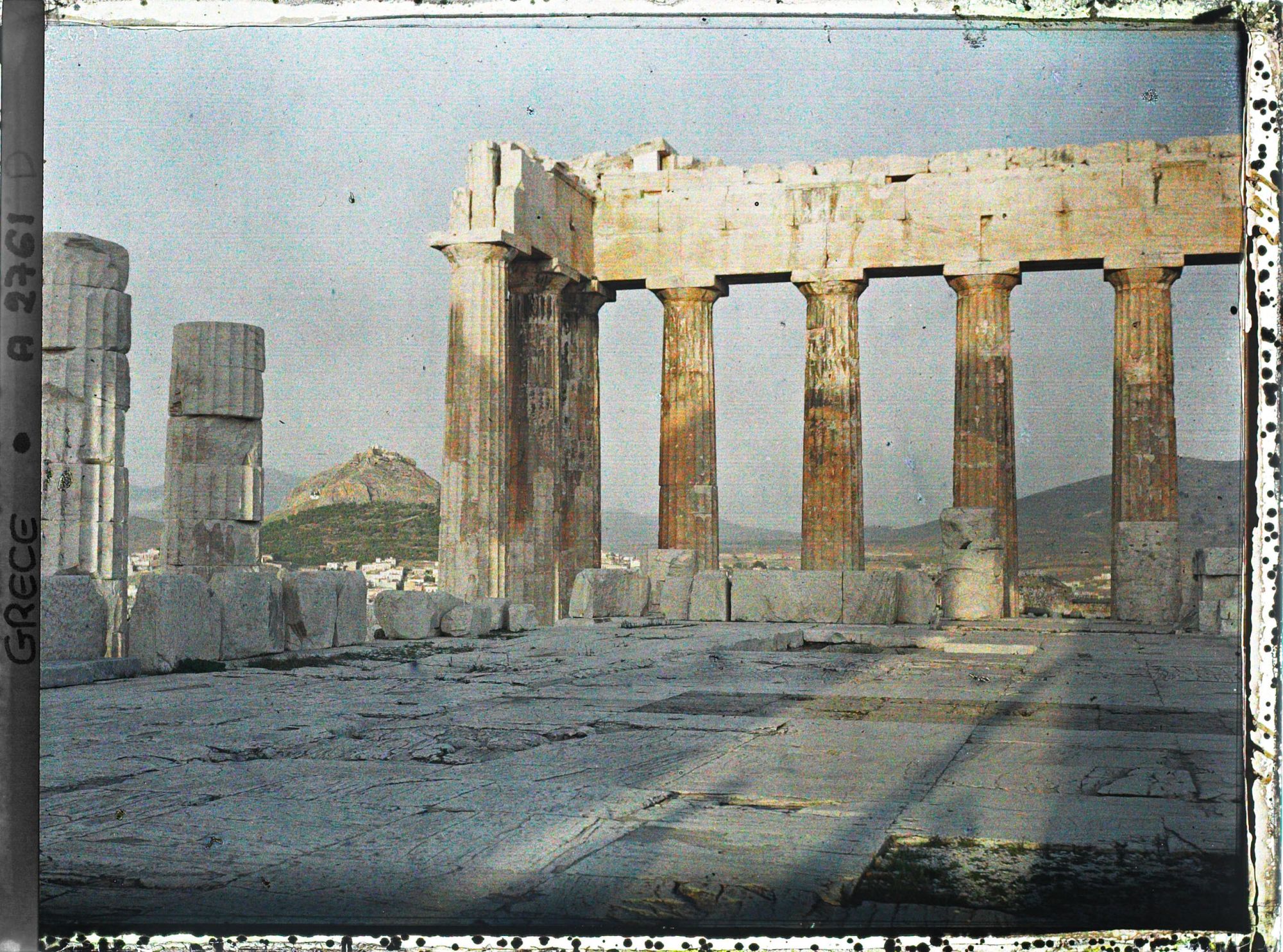 Image représentant Sur l'Acropole, le Parthénon. Vestiges de la colonnade extérieure côté est et derrière eux façade est de l'Acropole, la ville à ses pieds et le Mont Lycabette ("vue plongeante")