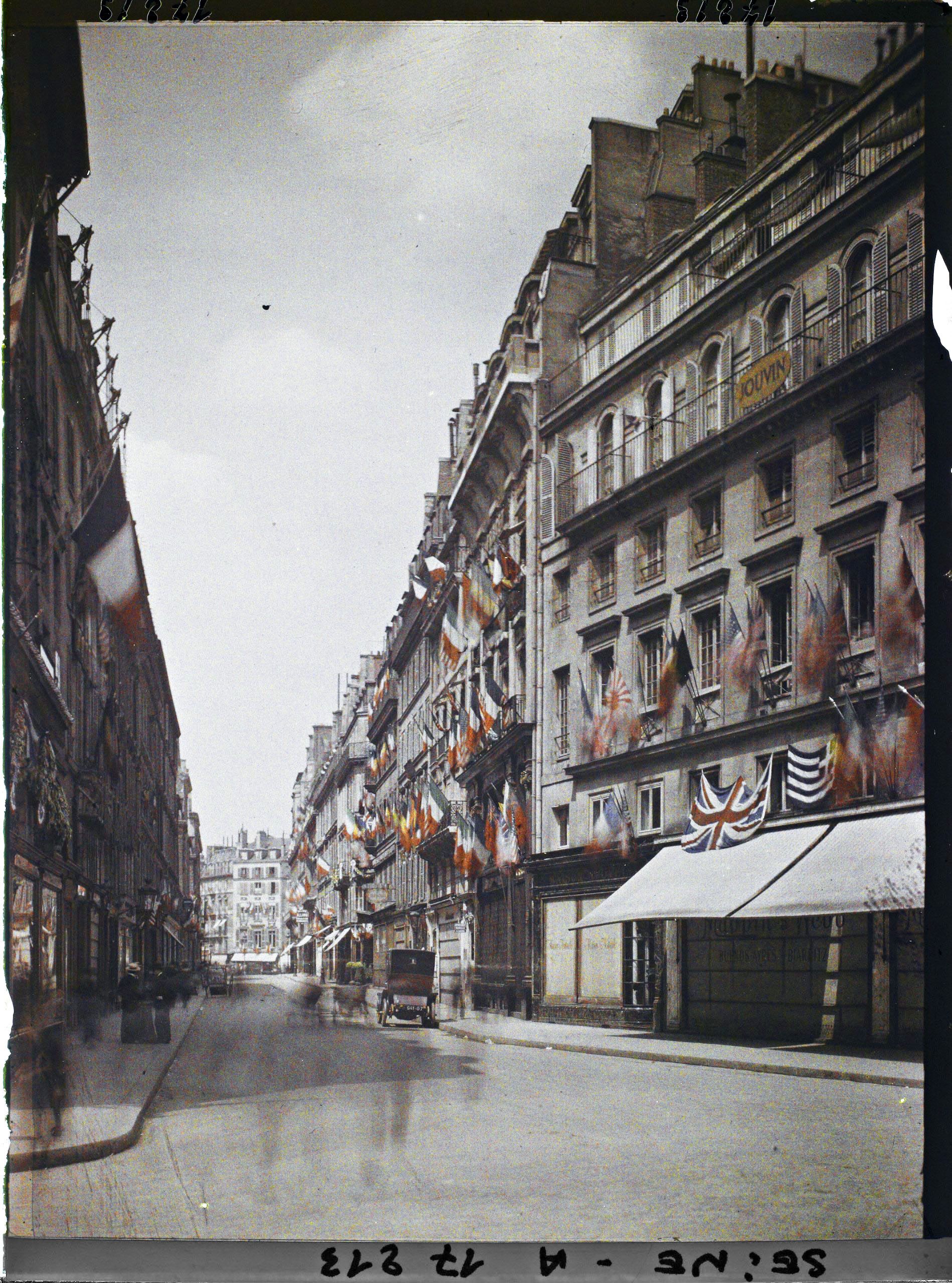 Image représentant La rue des Capucines vue de la rue de la Paix et décorée des drapeaux alliés pour les fêtes de la Victoire des 13 et 14 juillet 1919