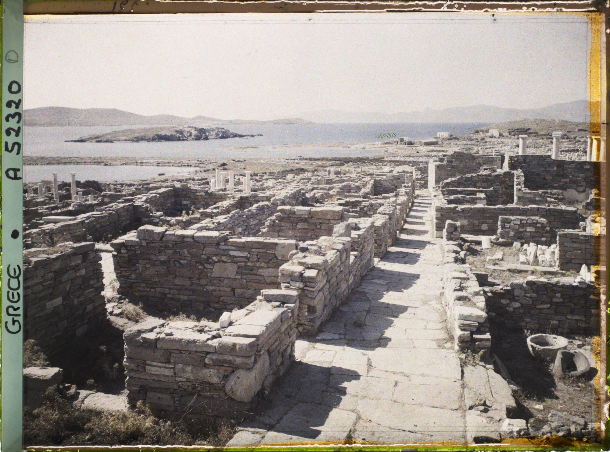 Image représentant La rue du Théâtre, vue vers la ville basse. Au fond, l'ile de Tinos