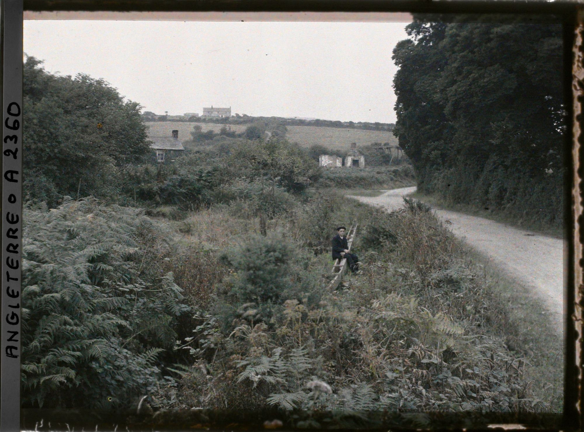 Image représentant Jeune homme assis vraisemblablement sur une canalisation en bois au bord d'une route