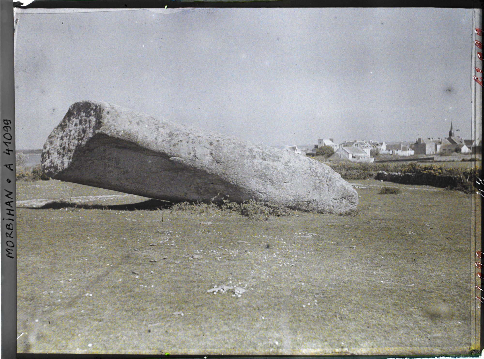 Image représentant Le plus gros des quatre morceaux du Grand Menhir brisé ; à l'arrière-plan, le village de Locmariaquer