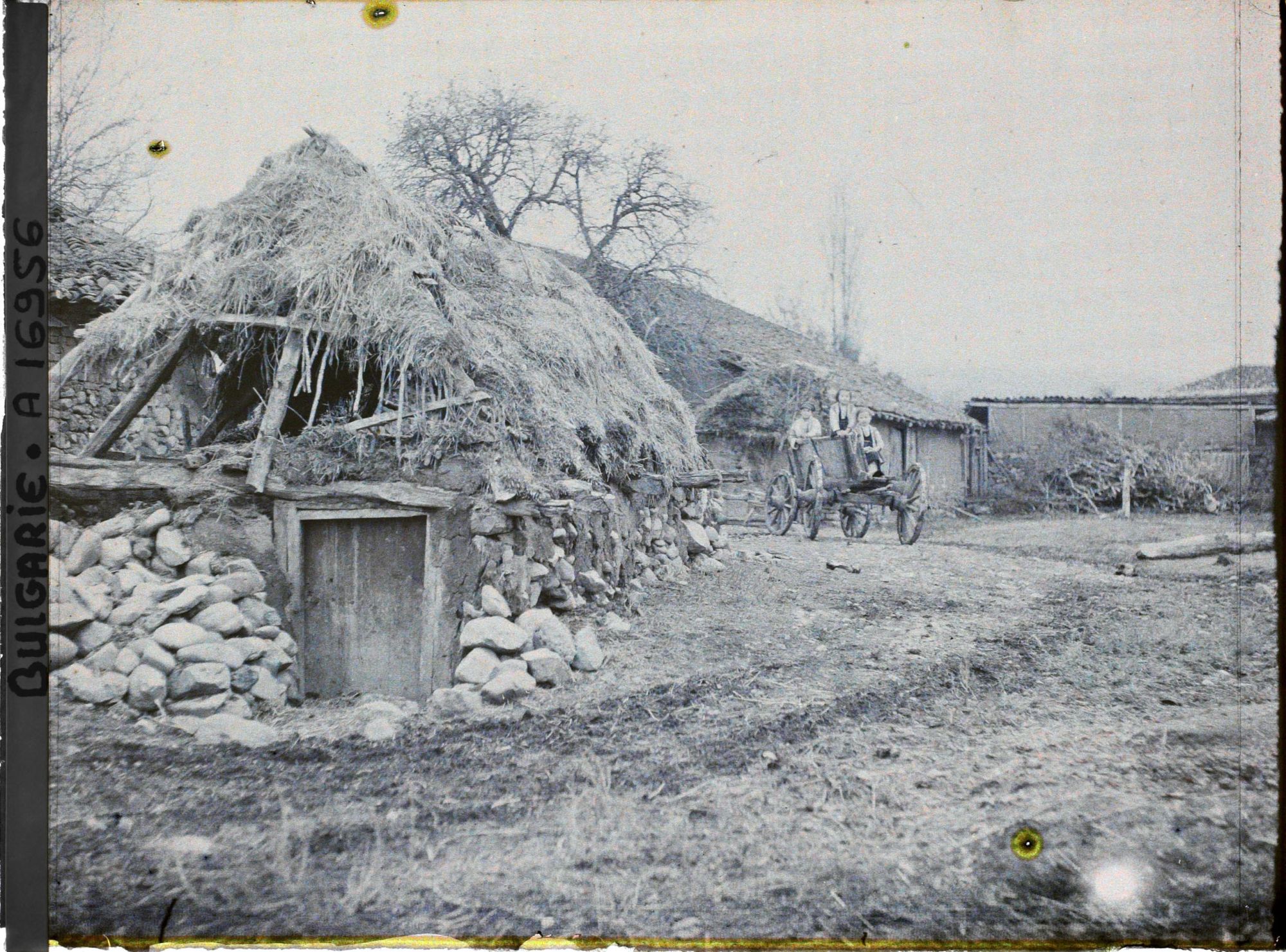 Image représentant Un silo (?) recouvert de chaume, bâtiments de ferme et trois enfants sur une carriole