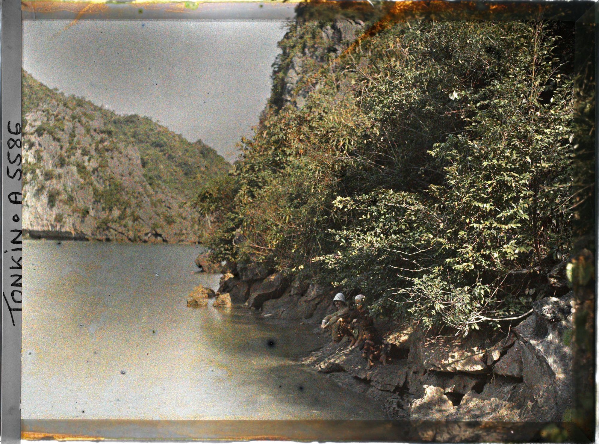 Image représentant Des Tonkinois et un occidental portant un casque colonial assis sur les rochers du cirque intérieur, près de " Port Bayard" (Groupe de la Surprise)