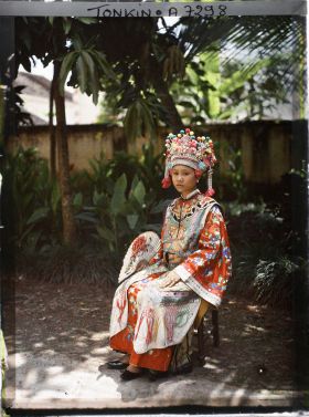 Image représentant Une actrice du Théâtre Saïgonnais, en costume de scène, éventail déployé à la main, assise dans un jardin