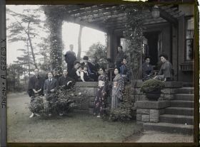 Image représentant groupe d'hommes, de femmes et d'enfants, les uns en tenue traditionnelle, les autres vêtus à l'occidentale (les hommes surtout) sur une terrasse.