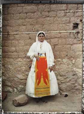 Image représentant Une villageoise en costume de cérémonie (robe blanche et tablier rouge bordée or)