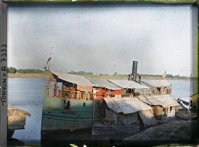 Image représentant Une chaloupe chinoise amarrée le long de maisons flottantes au bords du Fleuve Rouge, le soir