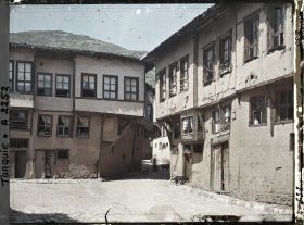 Image représentant Deux maisons presque identiques (l'une en bon état, l'autre moins) de part et d'autre d'une place pavée