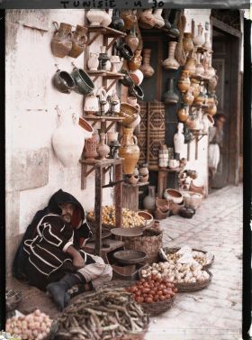 Image représentant Un marchand de fruits et légumes devant une boutique de poteries dans un souk de la médina