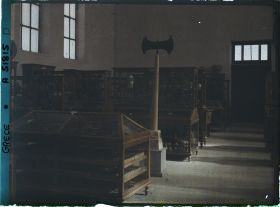 Image représentant Musée archéologique - Vitrines de bois contenant poteries et autres objets. Double hache sur un socle