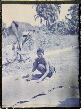 Image représentant Une jeune femme en sampot, torse nu, accroupie près d'une natte