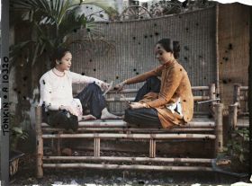 Image représentant Deux jeunes femmes saïgonnaises de classe aisée, jouant aux cartes assises sur une banquette en bambou