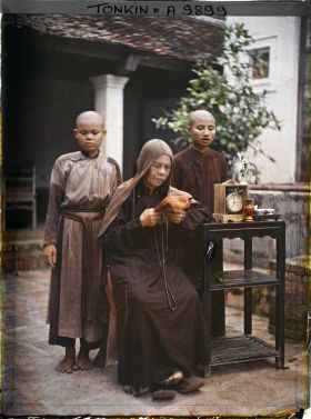 Image représentant Une bonzesse lisant devant deux novices, accoudée à une étagère supportant une pendulette, un vase et un service à thé