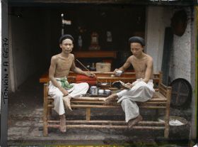 Image représentant Deux hommes prenant le thé, fumant la pipe à eau et lisant, assis sur une banquette en bambou