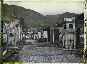 Image représentant Une rue bordée de bâtiments endommagés. A droite, une fontaine