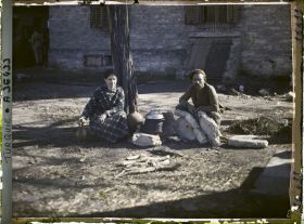 Image représentant Un homme et une jeune femme grecs s'apprêtant à quitter la ville prêt d'un foyer improvisé