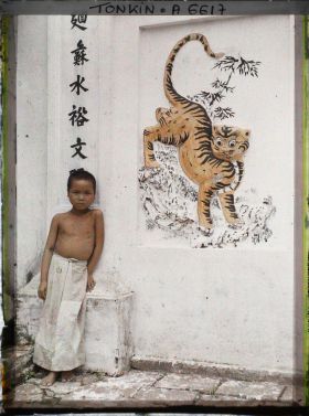 Image représentant Un enfant debout près d'un panneau décoratif peint représentant un tigre, dans la cour intérieure du temple dans le village de Vinh-thuy