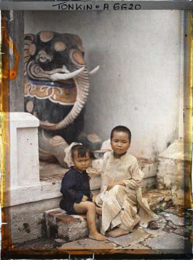 Image représentant Deux enfants assis devant une statue représentant un éléphant, à l'entrée du temple du village de Vinh-thuy
