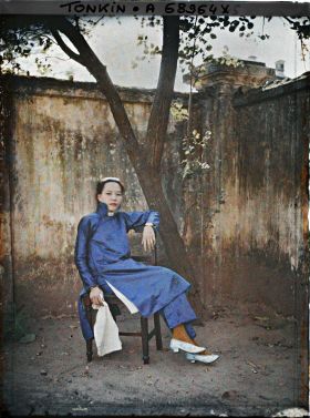 Image représentant Une métisse chinoise assise sur une chaise, de trois quarts, dans un angle de cour