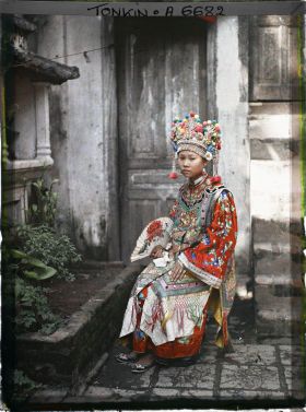 Image représentant Une actrice du Théâtre Saïgonnais, en costume de scène, assise devant une porte