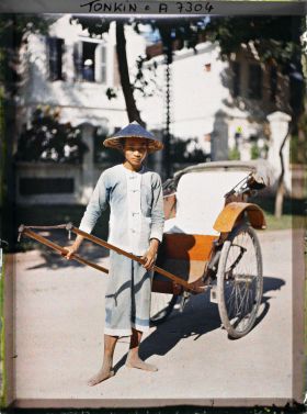 Image représentant Un pousse-pousse à roues caoutchoutées et son tireur, vêtu et coiffé de bleu