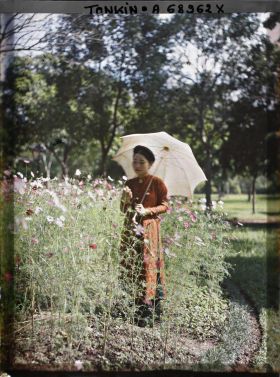 Image représentant Une jeune femme de classe aisée, s'abritant sous une ombrelle blanche, dans un massif de cosmos d'un jardin public