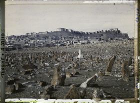 Image représentant Vers la ville surmontée de sa citadelle. Au premier plan, pierre tombale de l'un des cimetières entourant la ville