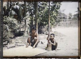Image représentant Une jeune femme accroupie près d'une natte et un enfant pilonnant du riz
