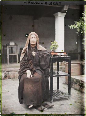 Image représentant Une bonzesse accoudée à une étagère supportant un vase et un service à thé dans la cour intérieure du temple Vien-minh